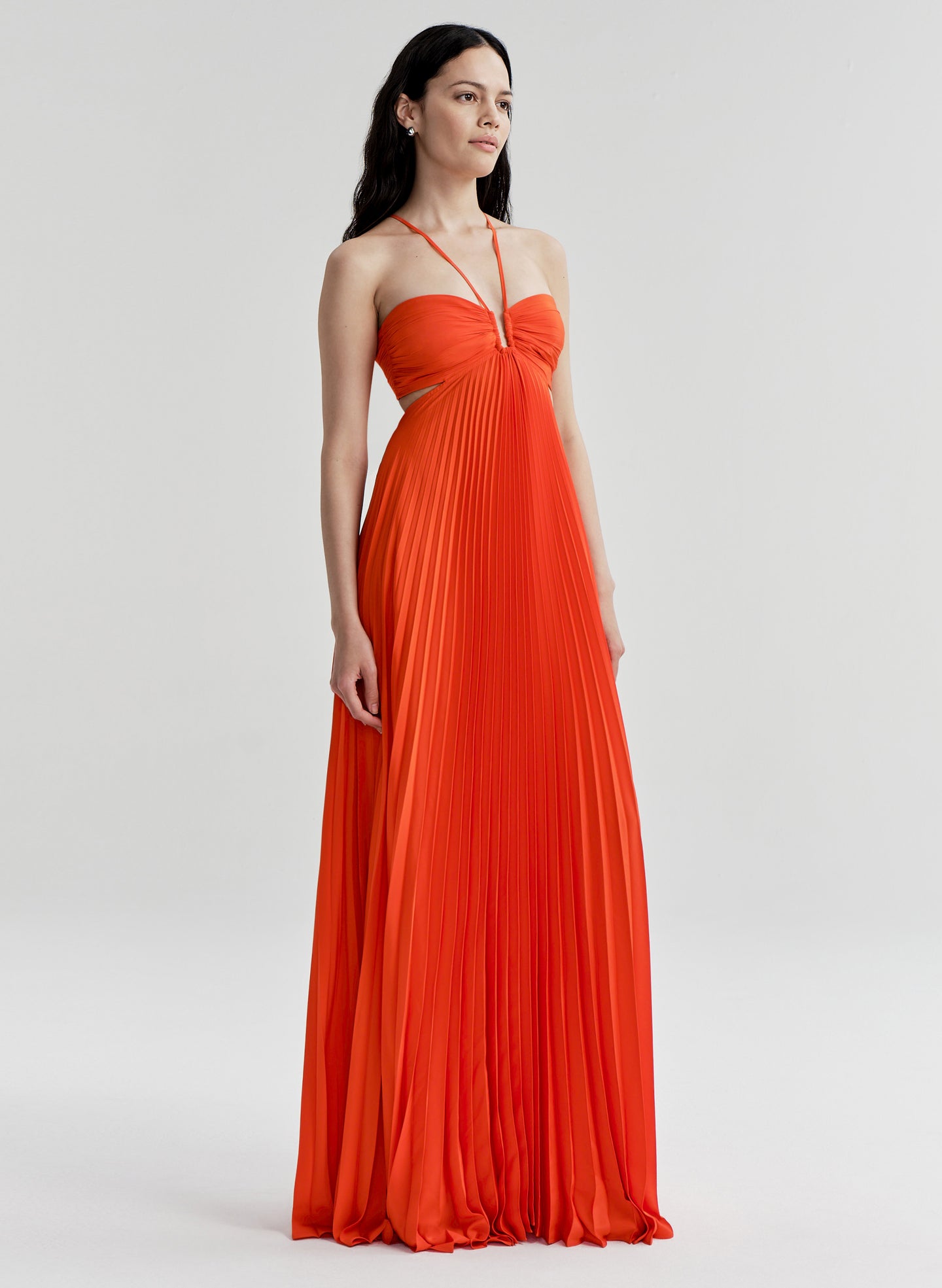 Woman wearing a bright orange halter neck gown on a white background
