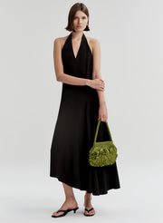 woman wearing black dress carrying green raffia shoulder bag