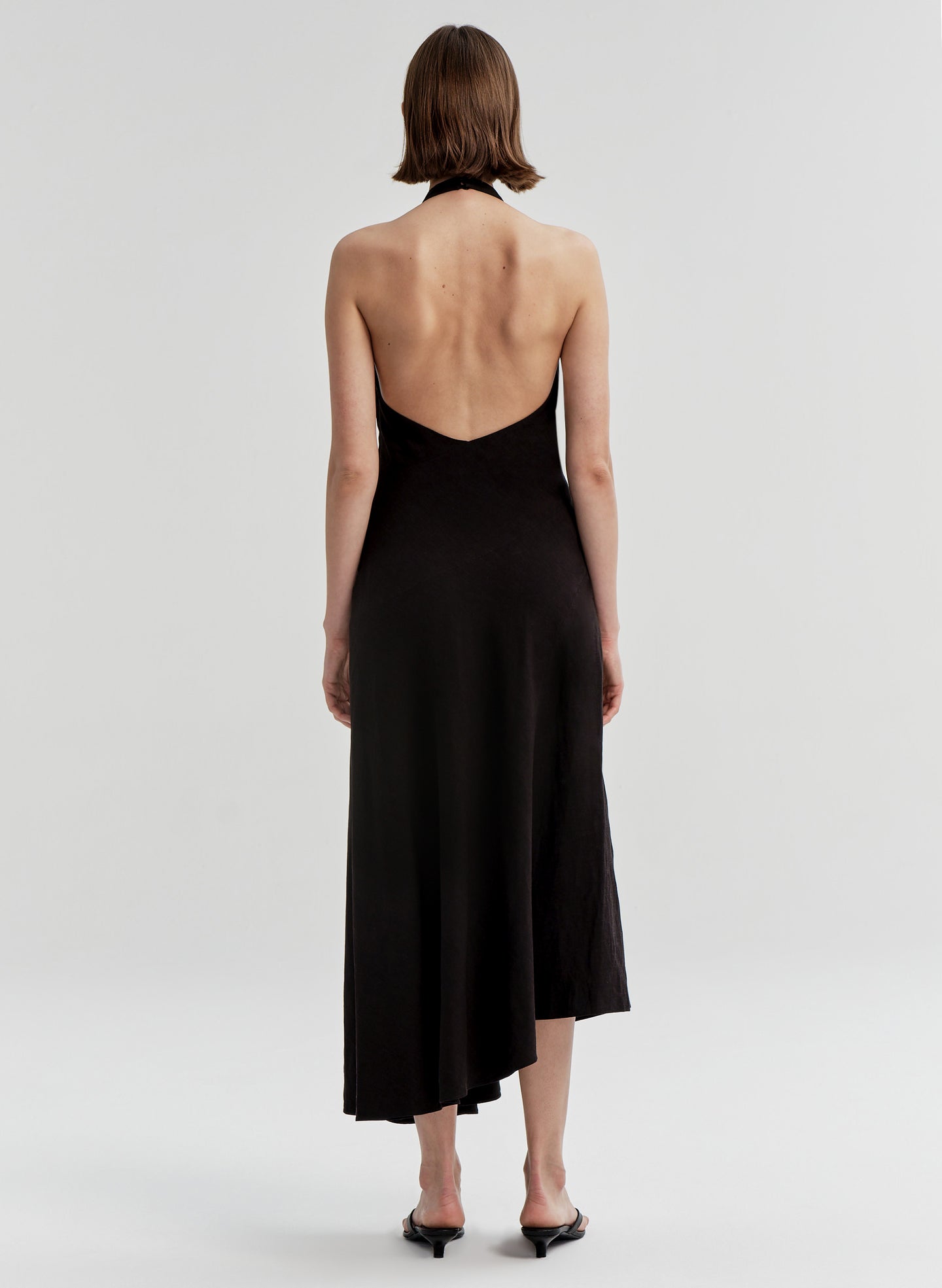 Woman wearing a black halter neck dress with an open back on a white background