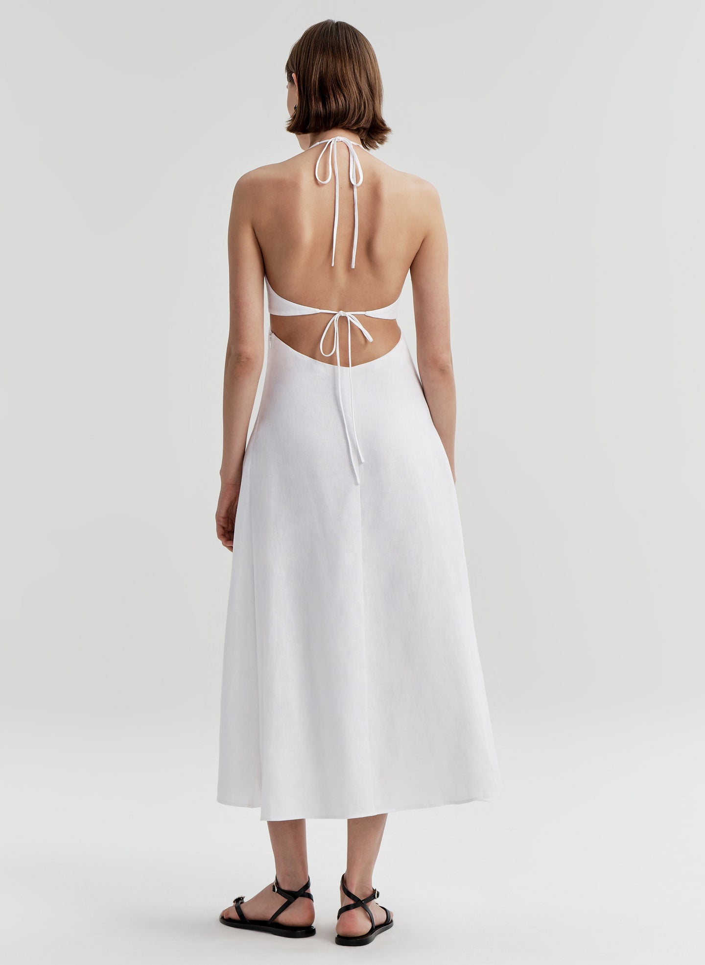 Woman wearing a white dress with cut-out back on a light gray background