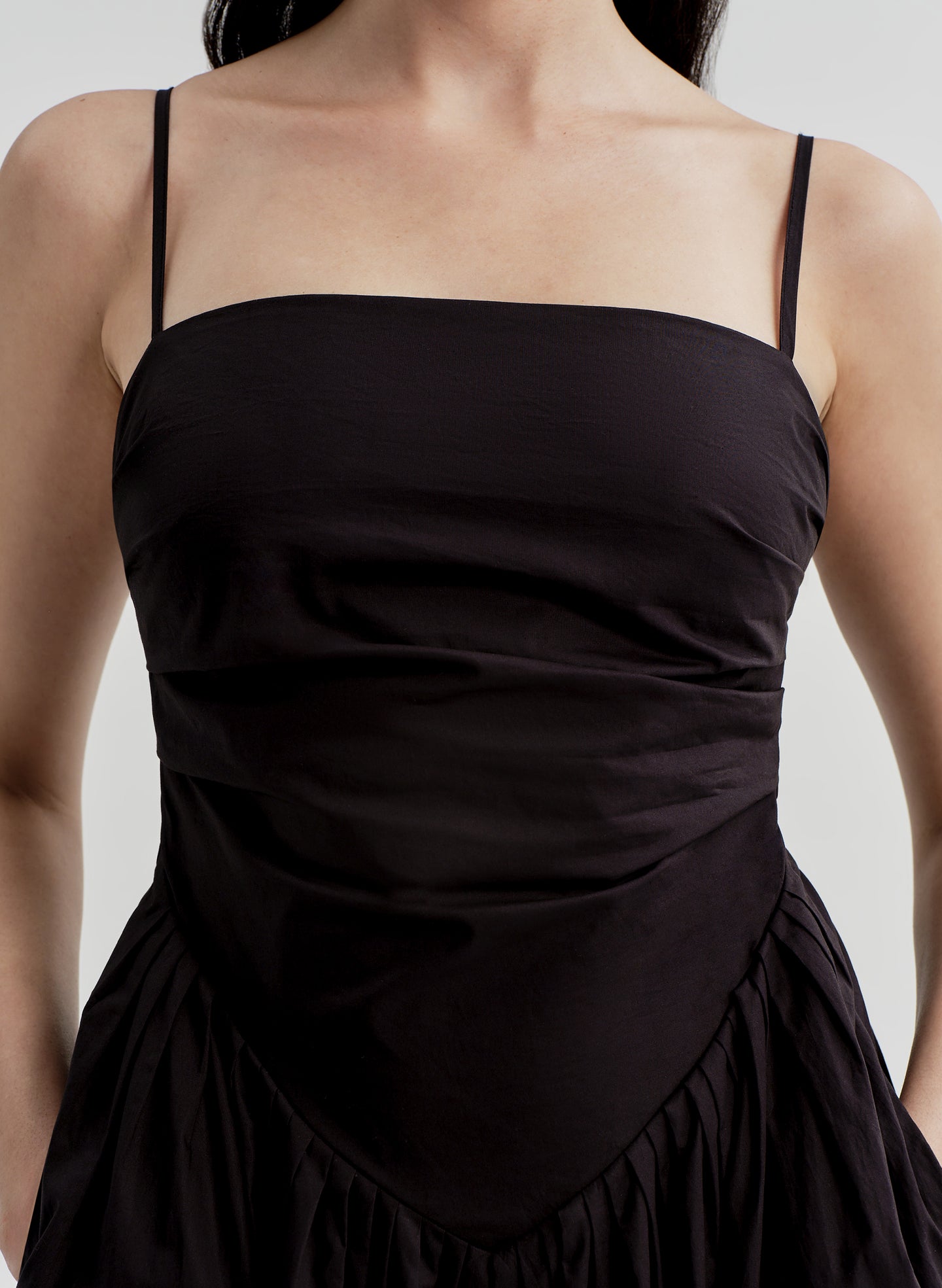 Woman wearing a black dress with thin straps on a plain background
