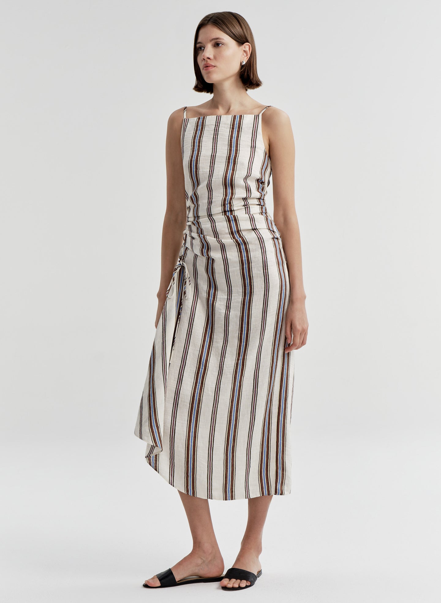 Woman wearing a sleeveless linen dress with brown and blue striped pattern on a white background