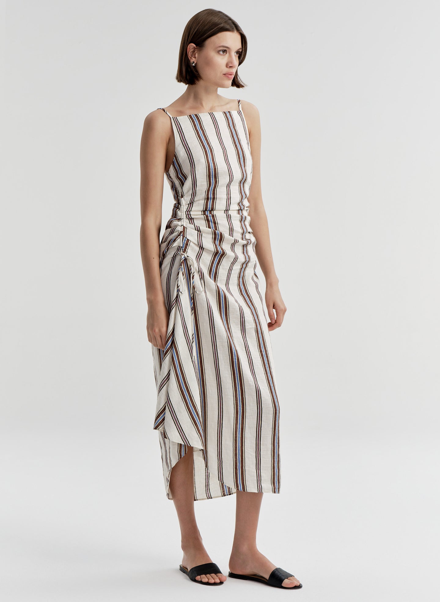 Woman wearing a sleeveless linen dress with brown and blue striped pattern on a white background