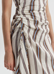 Woman wearing a sleeveless linen dress with brown and blue striped pattern on a white background