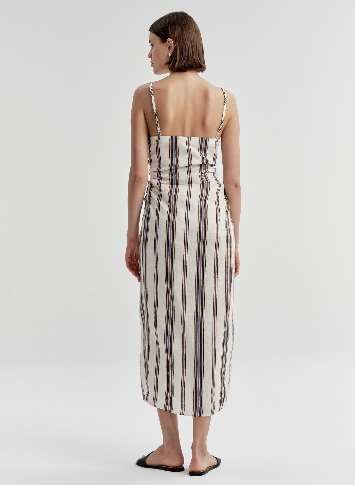Woman wearing a sleeveless linen dress with brown and blue striped pattern on a white background