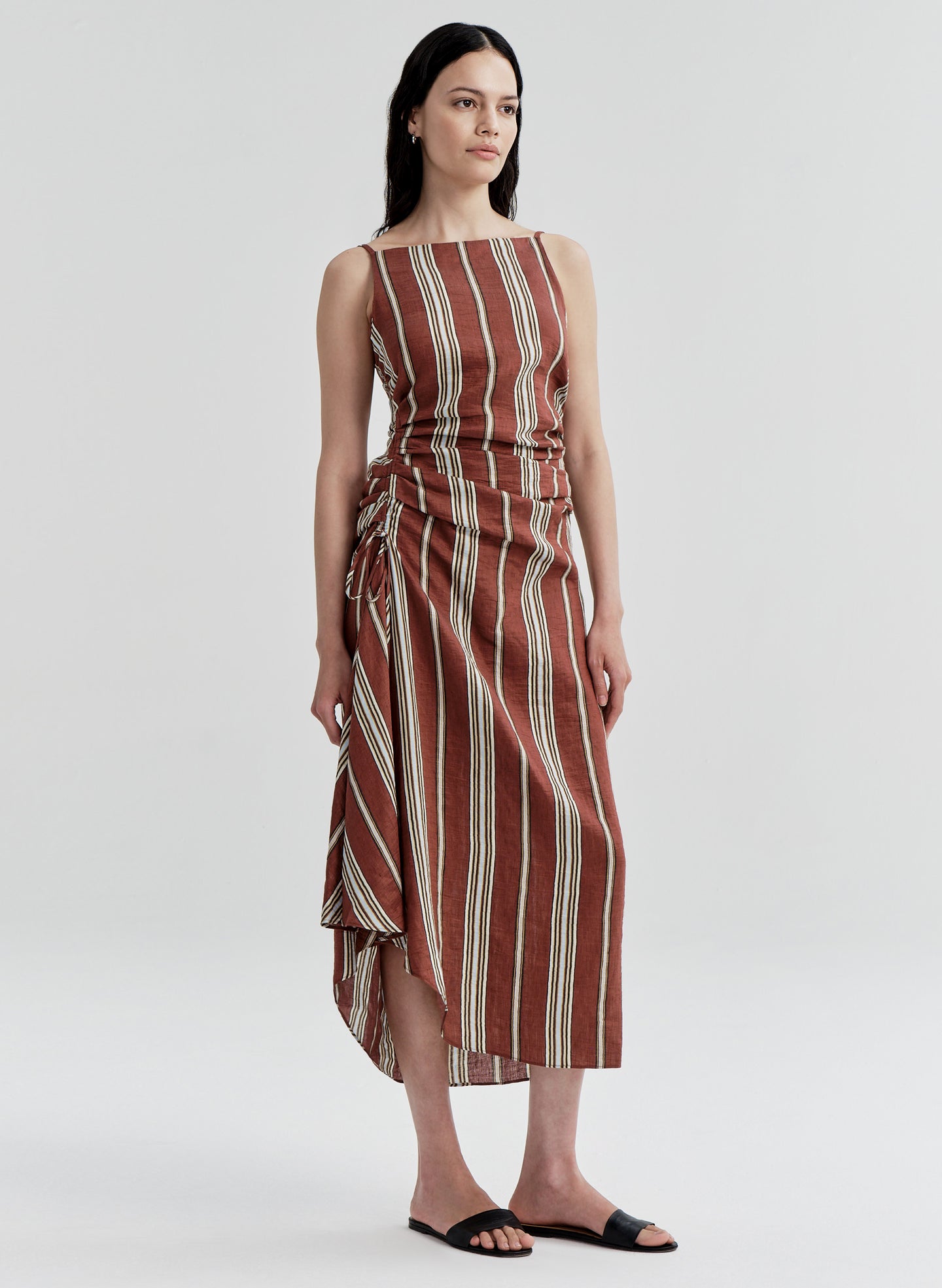 Woman wearing a linen brown and beige striped dress on a white background