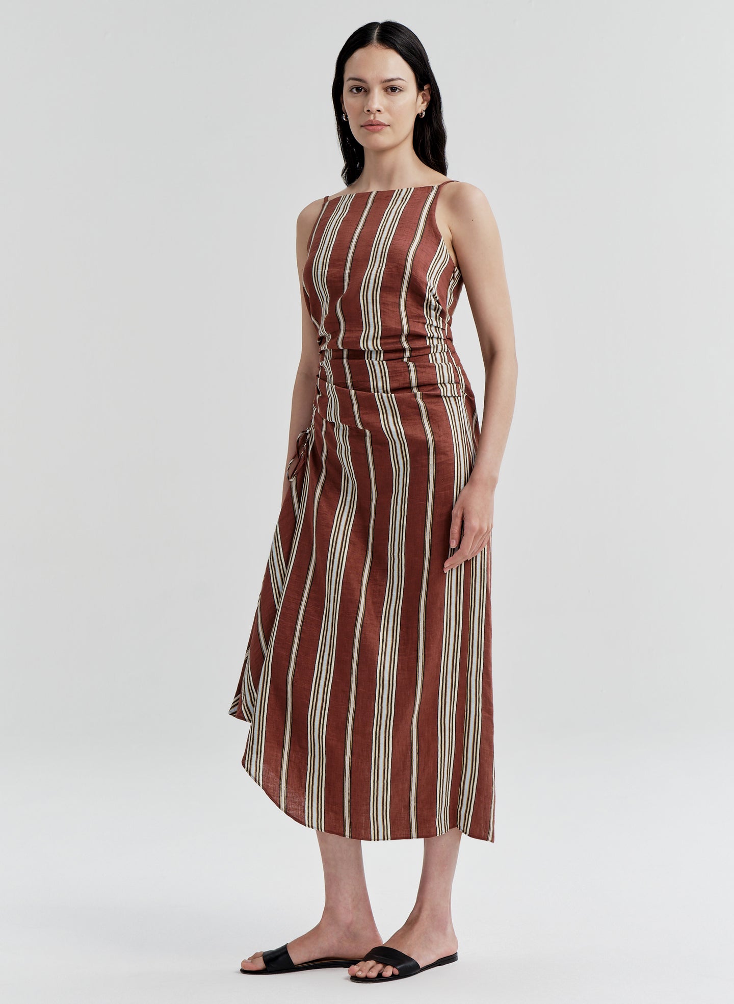 Woman wearing a linen brown and beige striped dress on a white background
