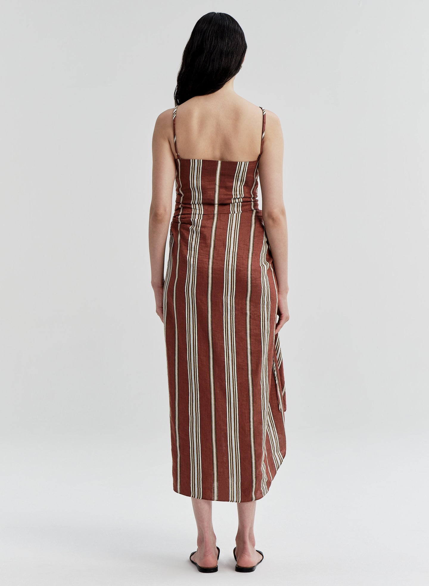 Woman wearing a linen brown and beige striped dress on a white background