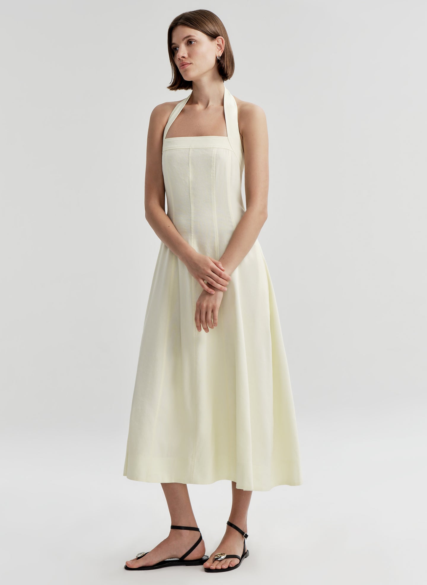 Woman wearing a beige halter neck dress on a plain background