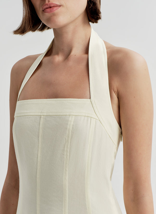 Woman wearing a beige halter neck dress on a plain background