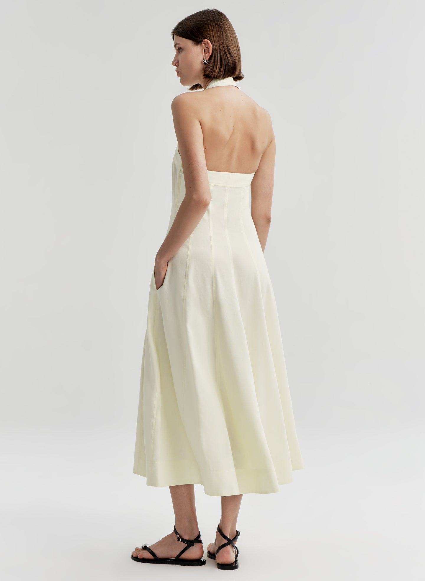 Woman wearing a beige halter neck dress with an open back on a plain background