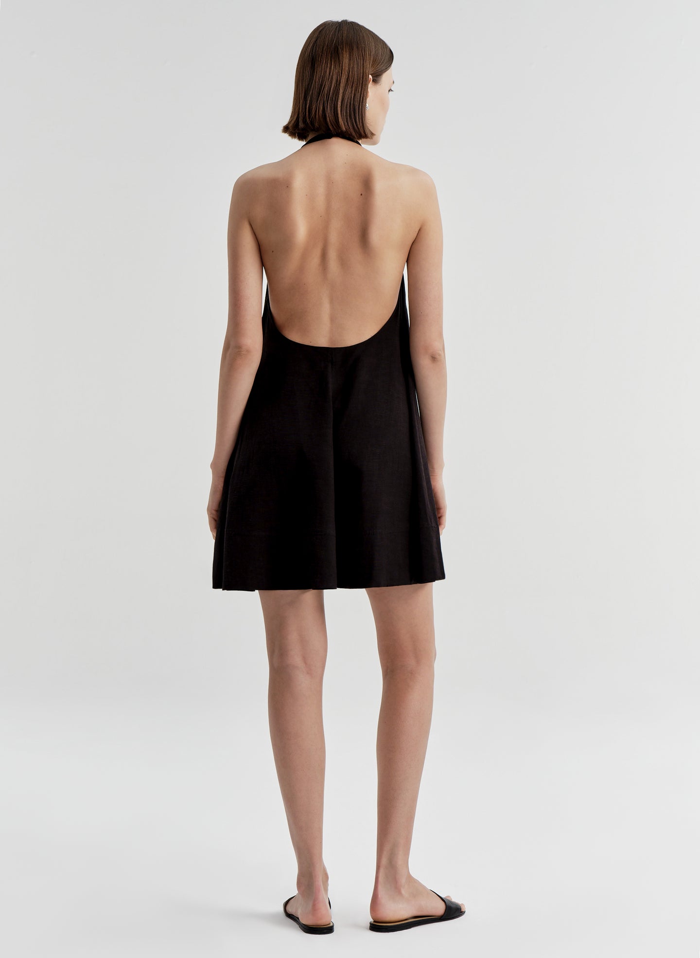 Woman wearing a black halter neck dress with an open back on a light gray background
