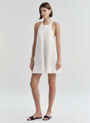 Woman wearing a white halter neck dress on a plain background