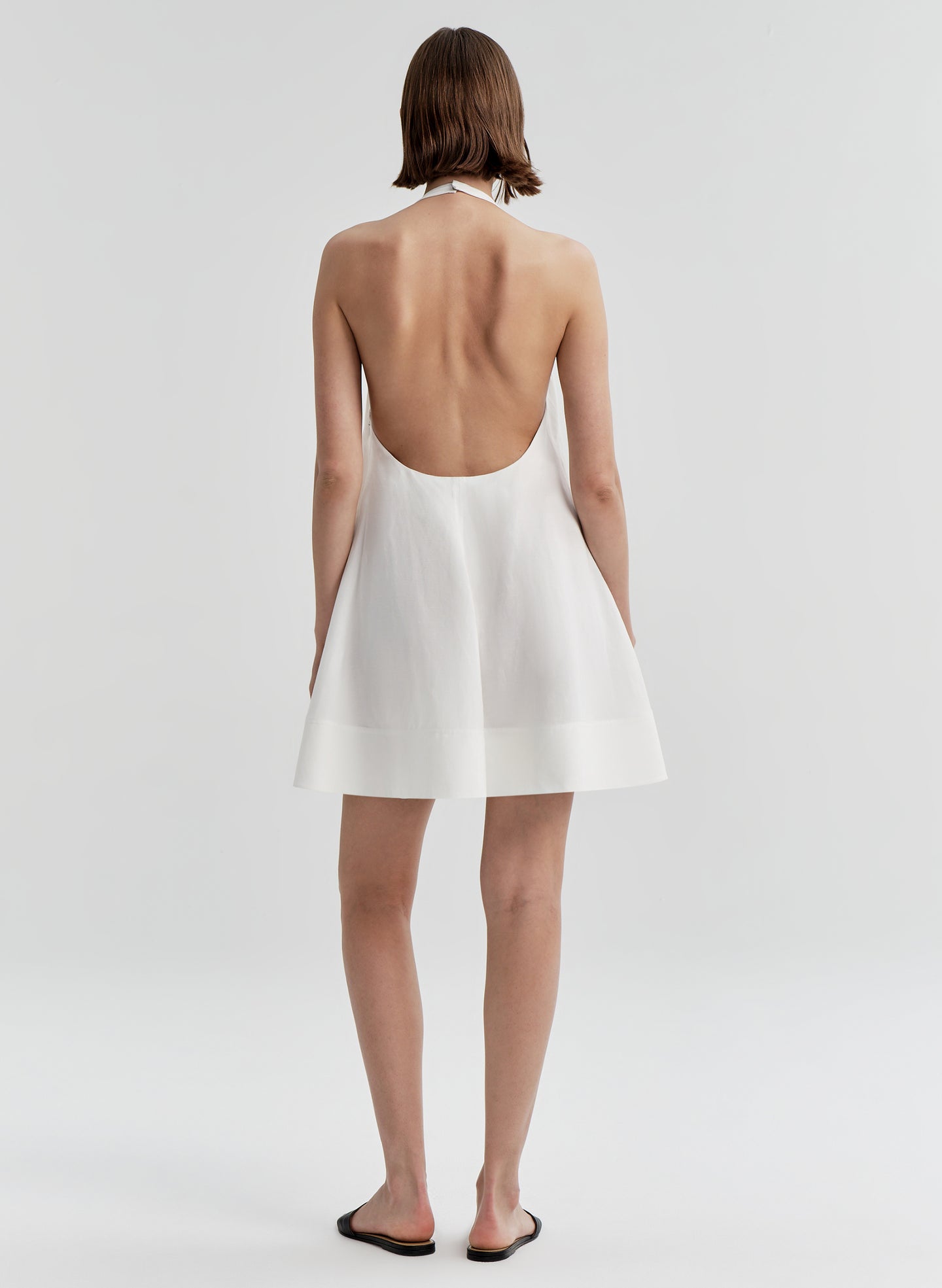 Woman wearing a white halter dress with an open back on a light gray background