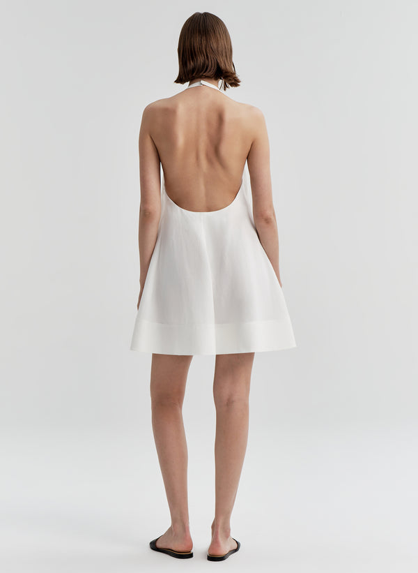 Woman wearing a white halter dress with an open back on a light gray background