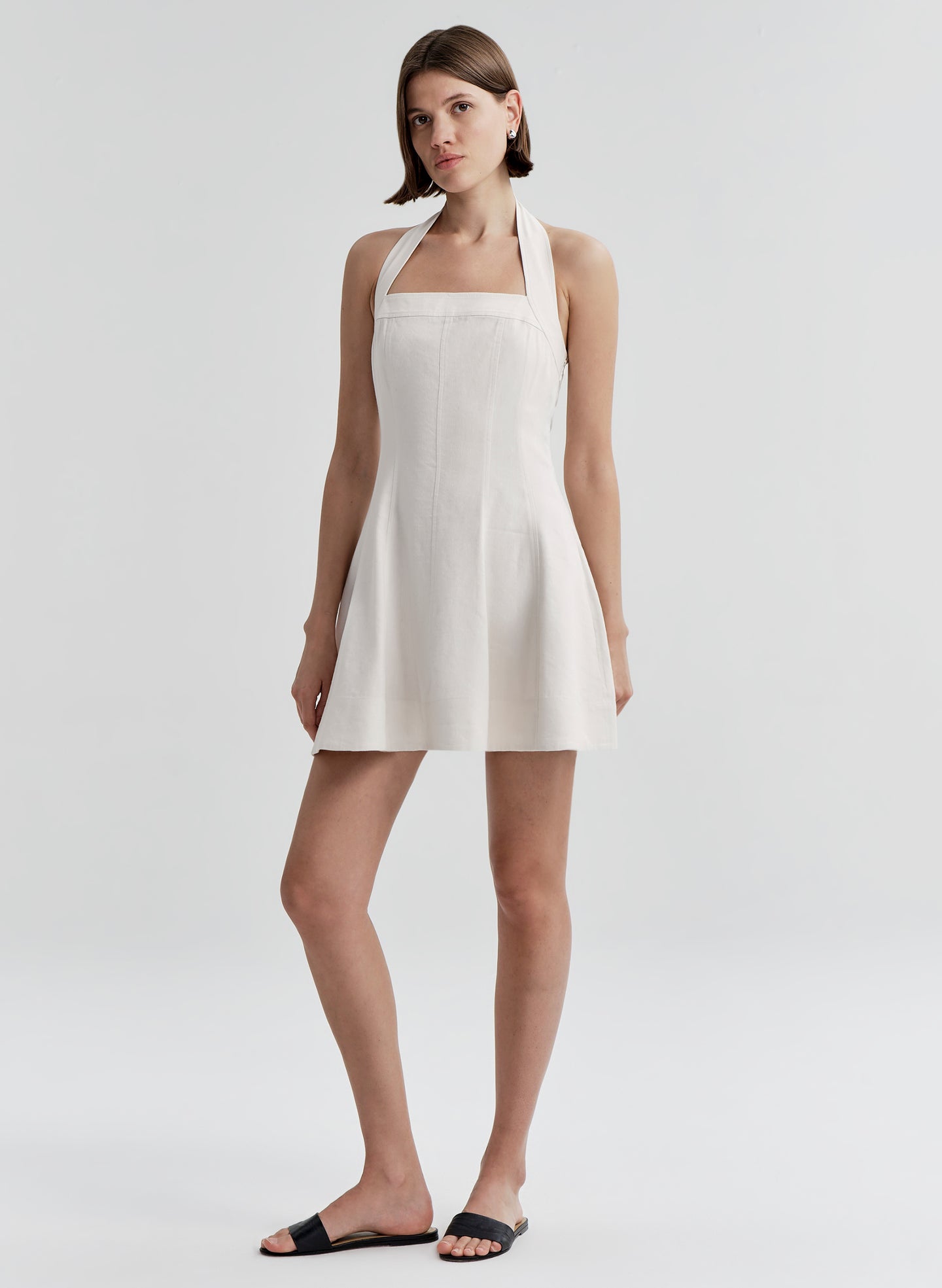 Woman wearing a beige linen halter neck dress on a plain background