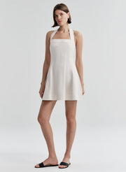 Woman wearing a beige linen halter neck dress on a plain background