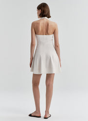 Woman wearing a beige linen halter neck dress with an open back on a plain background