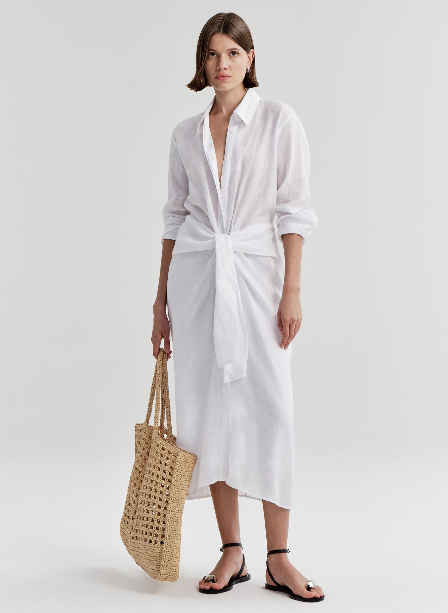 Woman wearing a white shirt dress with a knot detail on a white background