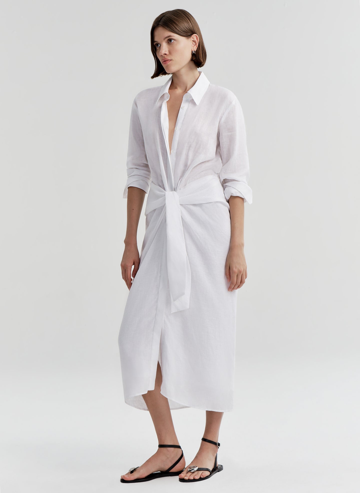 Woman wearing a white shirt dress with a knot detail on a white background