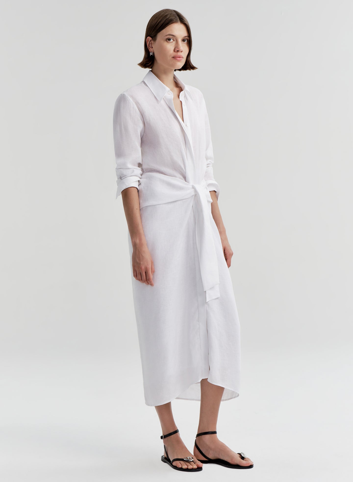 Woman wearing a white shirt dress with a knot detail on a white background