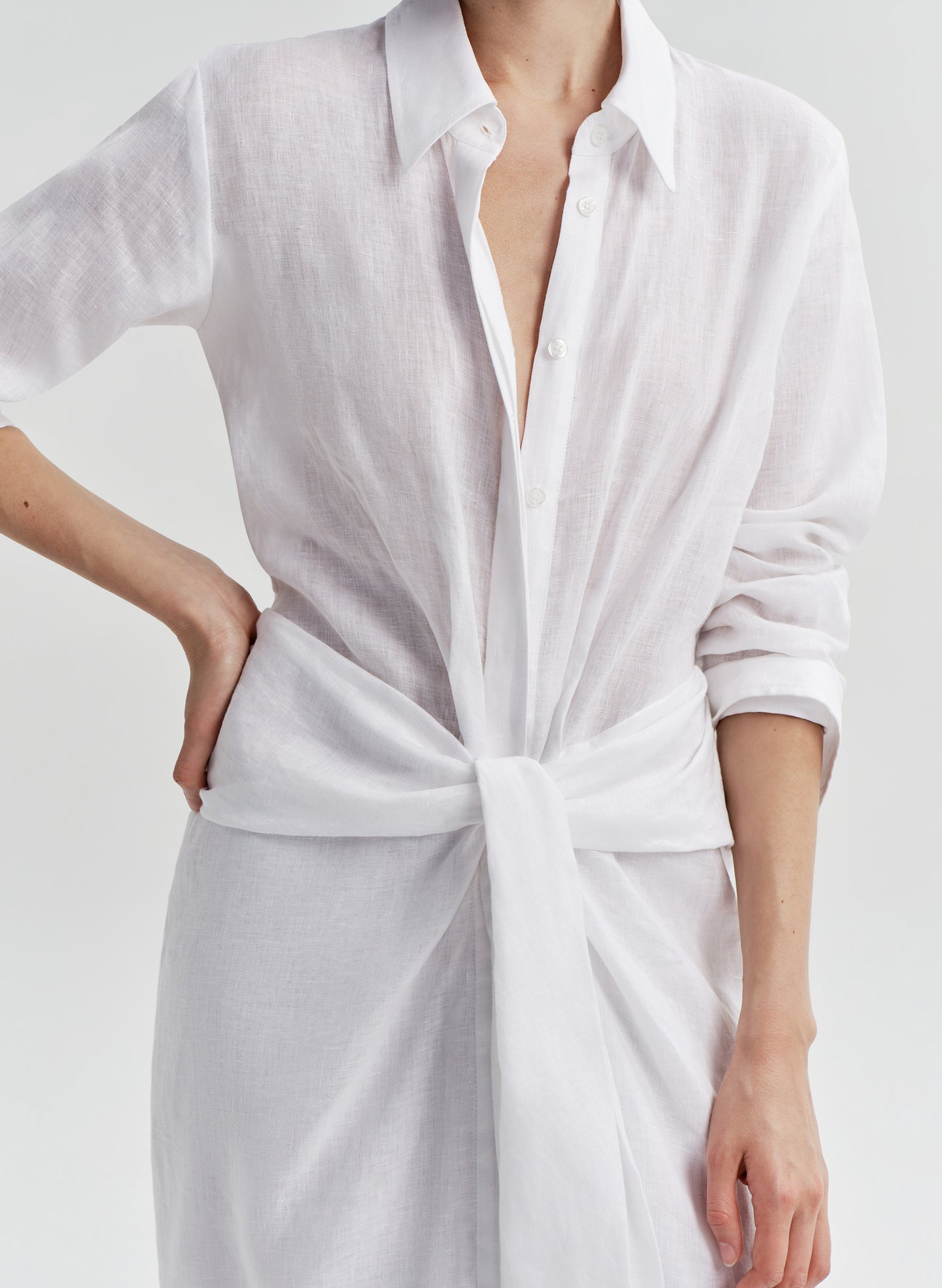 Woman wearing a white shirt dress with a knot detail on a white background