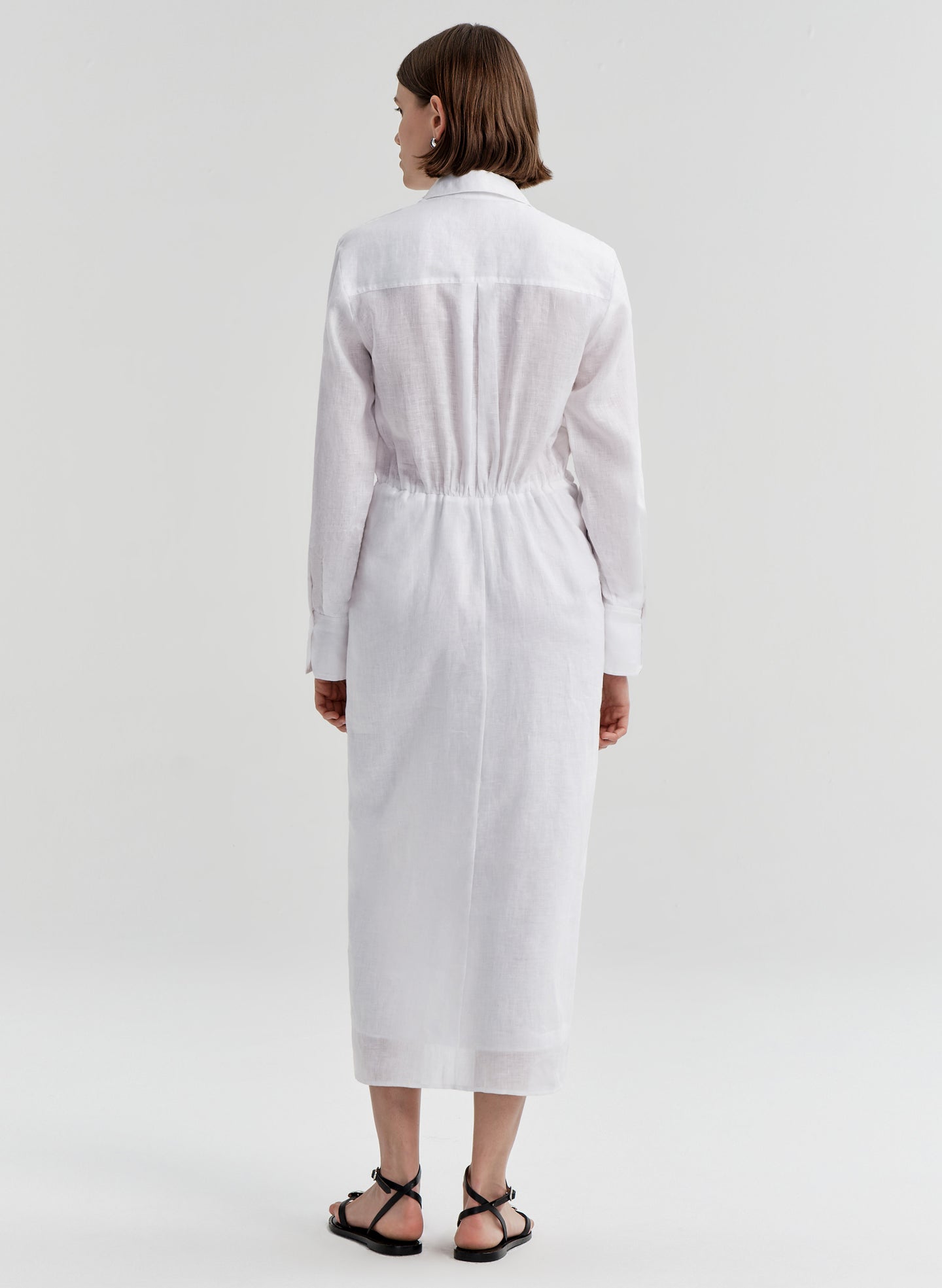 Woman wearing a white shirt dress with a knot detail on a white background