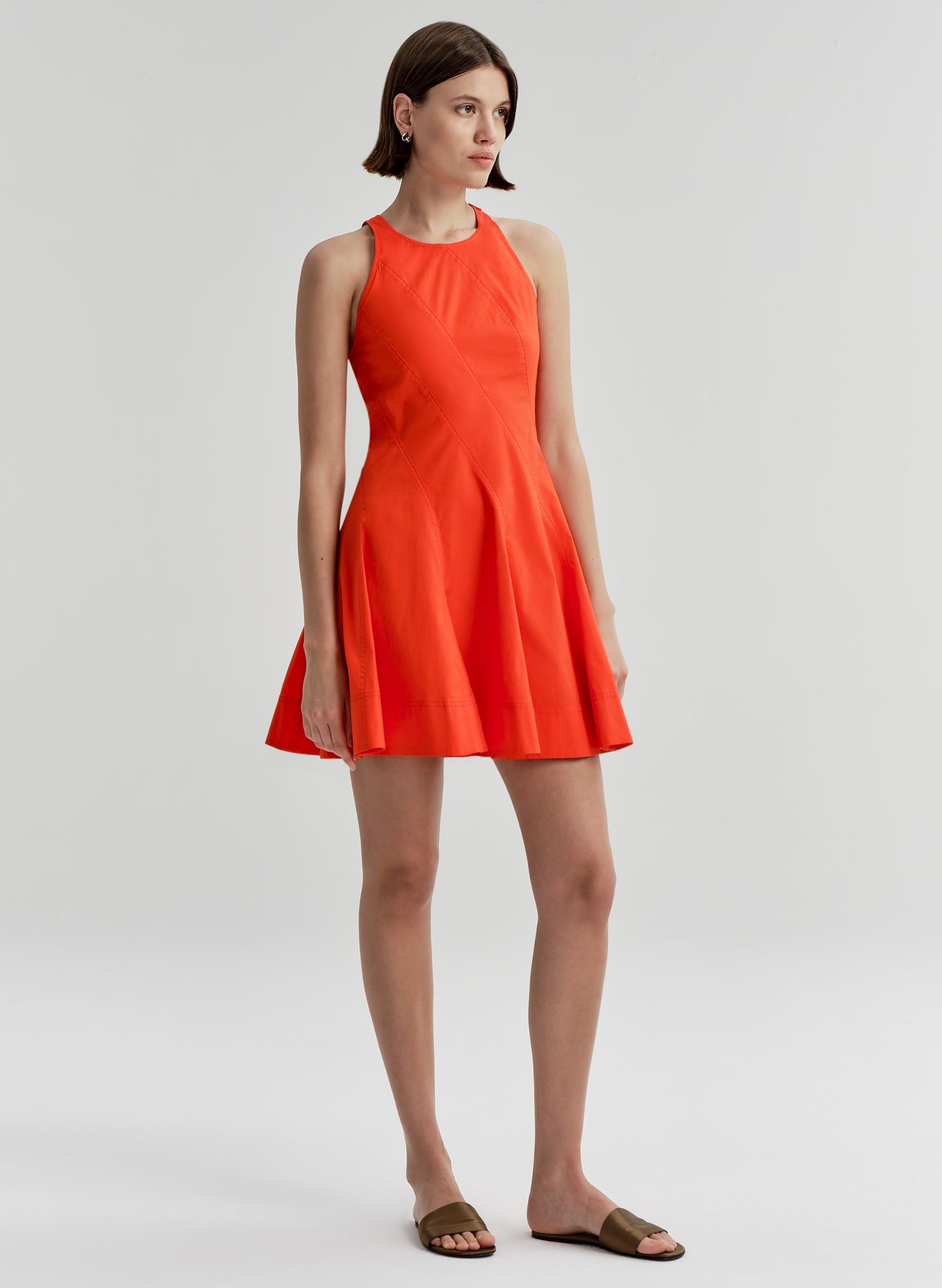 Woman wearing a bright orange sleeveless dress on a white background