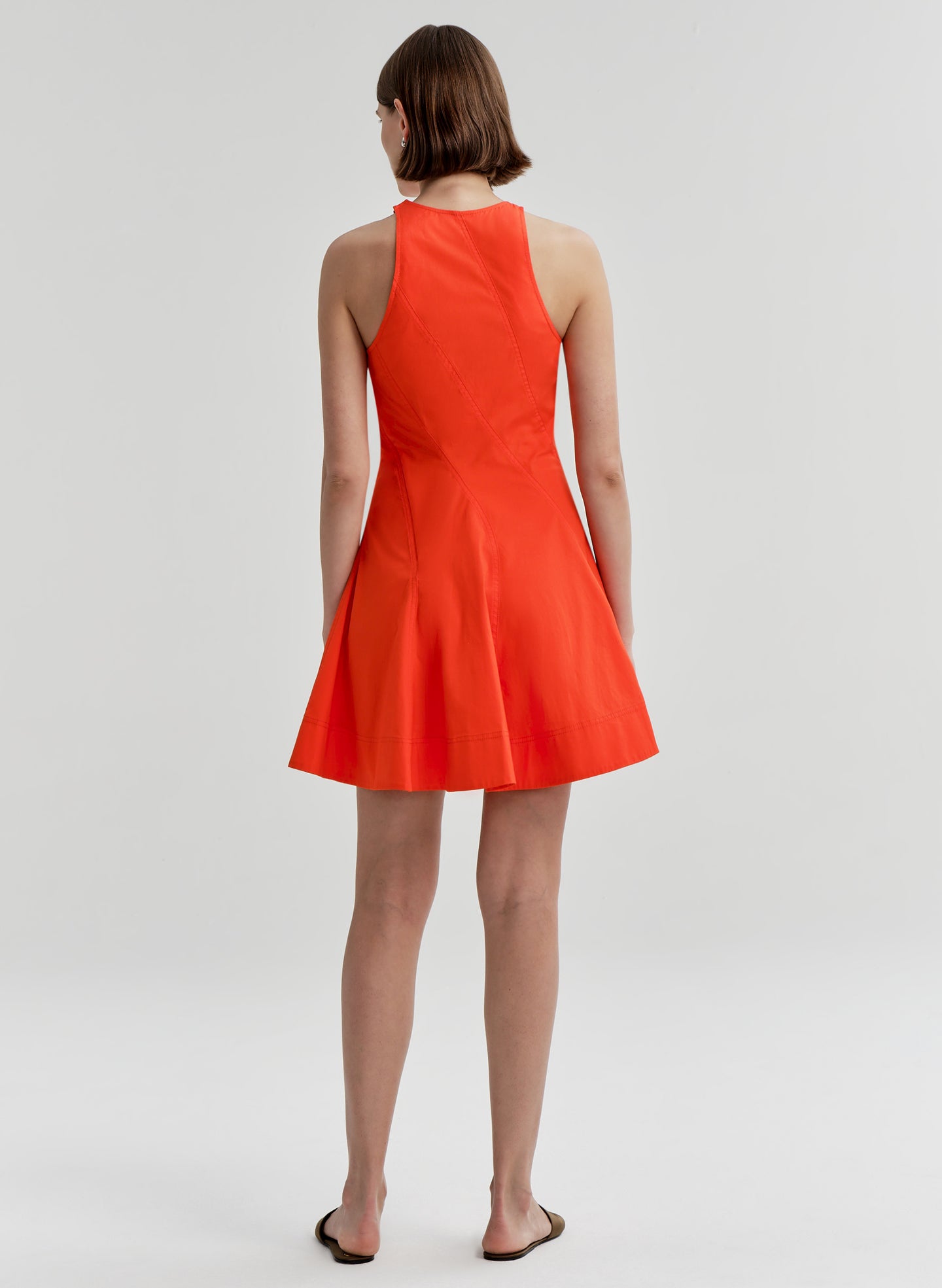 Woman wearing a bright orange sleeveless dress on a white background