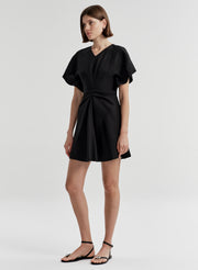Woman wearing a black dress with a knot detail on a plain background