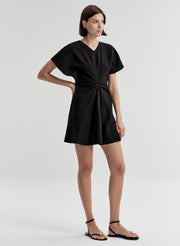 Woman wearing a black dress with a knot detail on a plain background