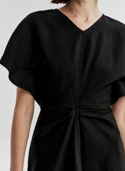 Woman wearing a black dress with a knot detail on a plain background