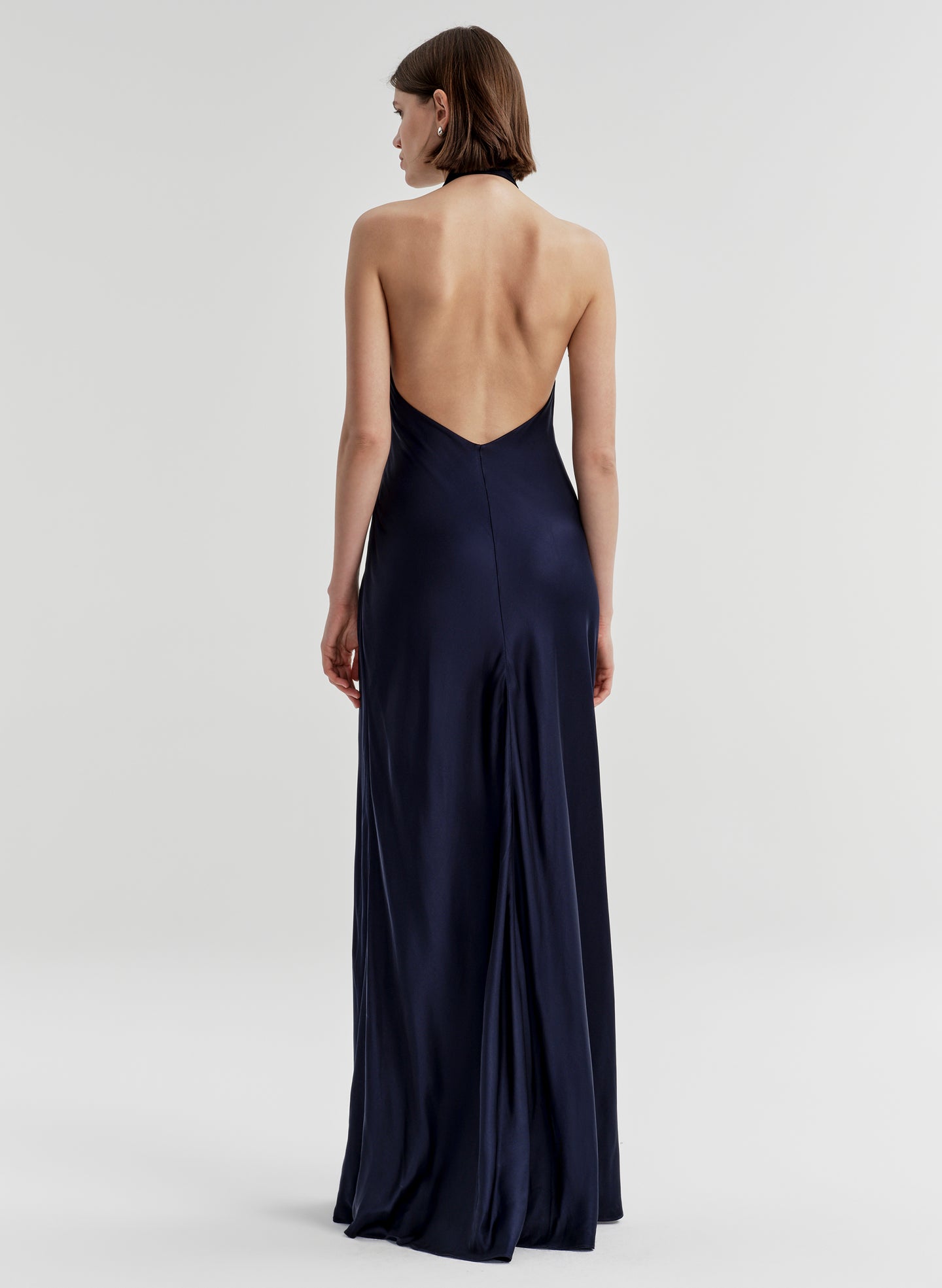 Woman wearing a navy blue halter neck gown with an open back on a white background