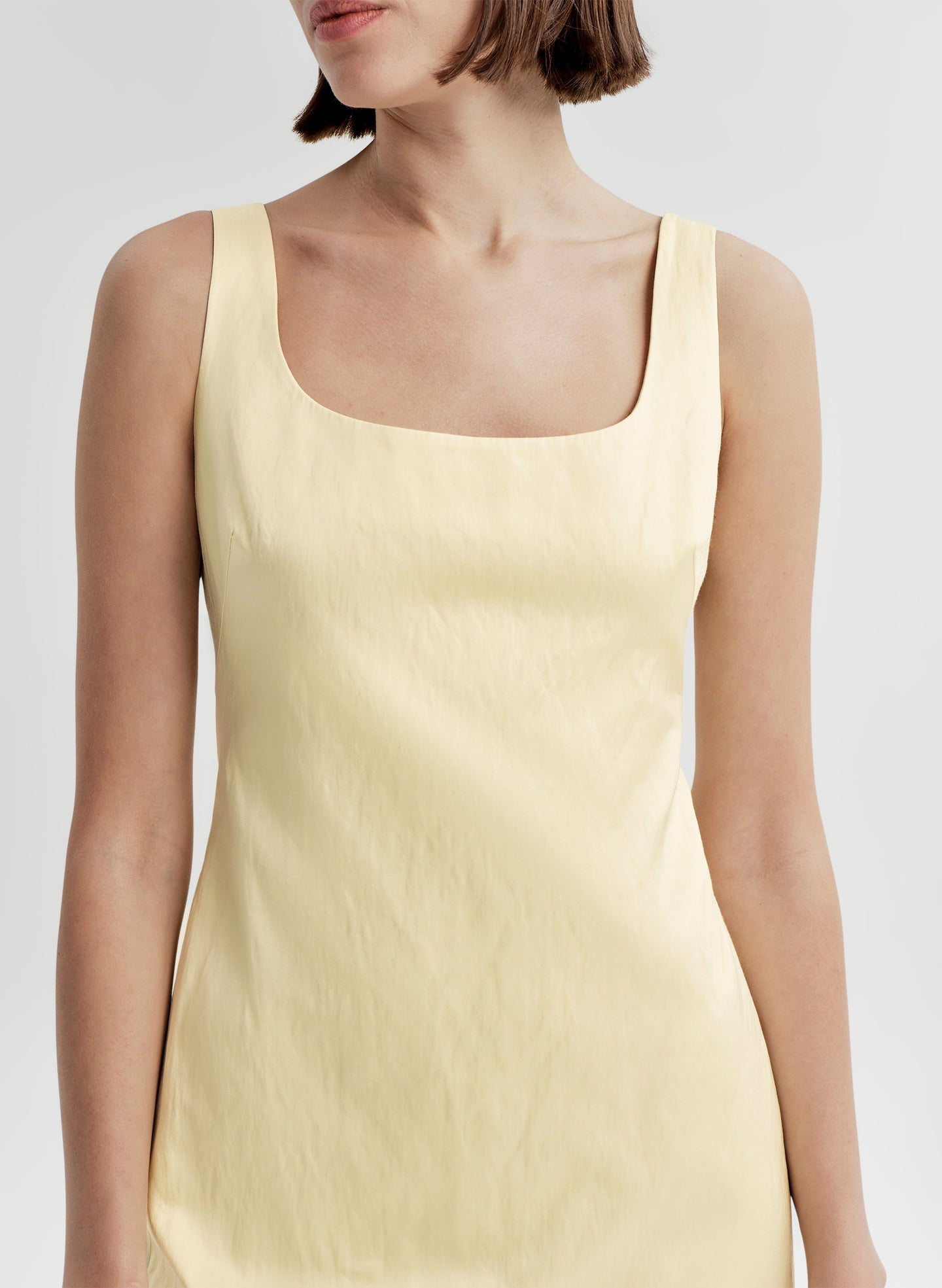 Woman wearing a light yellow tank dress against a plain background
