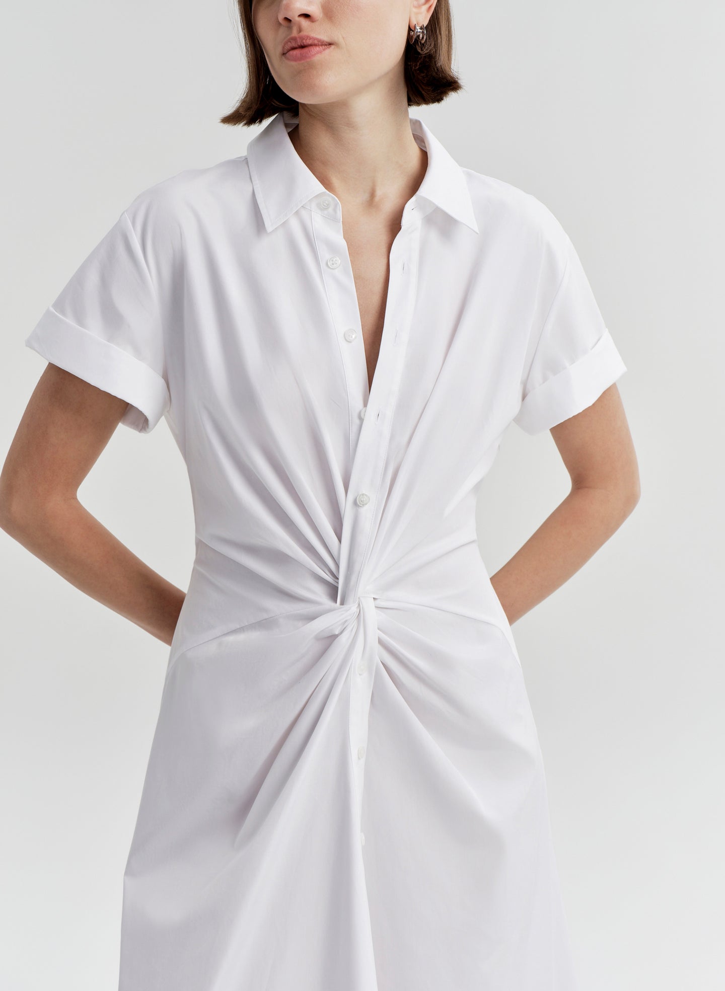 Woman wearing a white short-sleeve dress with a knot detail on a light gray background