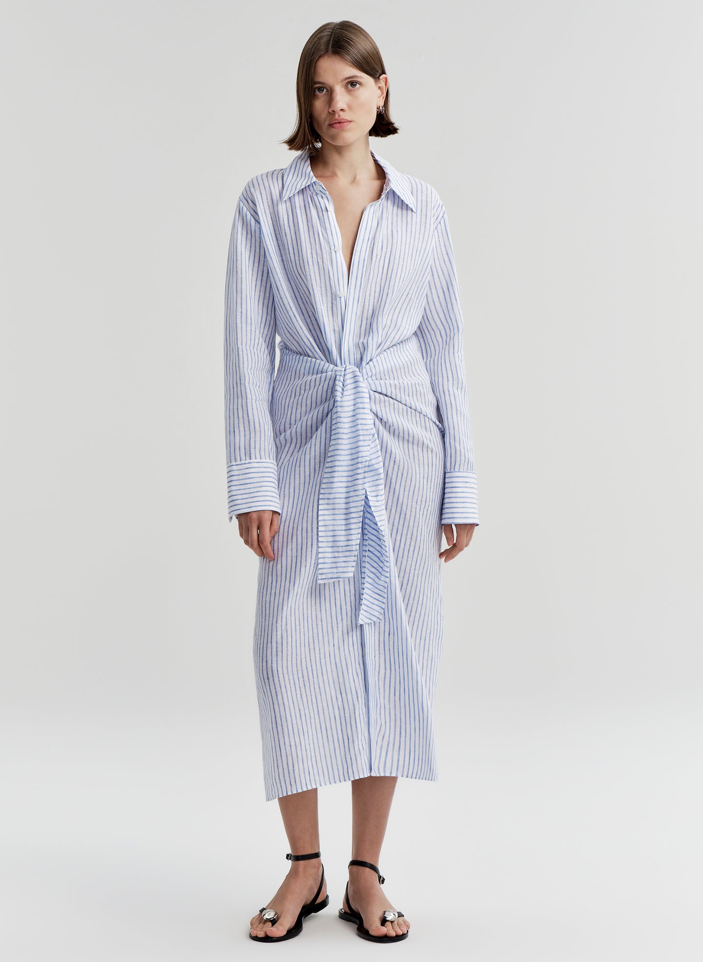 Woman wearing a blue and white striped dress with a knot detail on a plain background