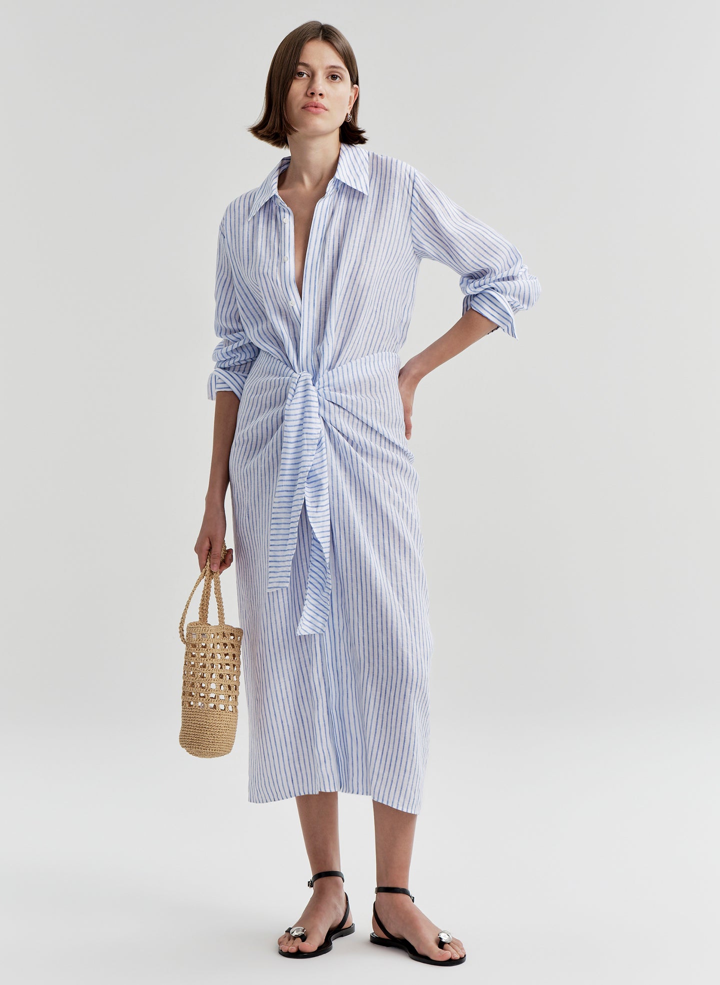 Woman wearing a blue and white striped dress with a knot detail on a plain background