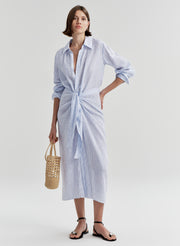 Woman wearing a blue and white striped dress with a knot detail on a plain background