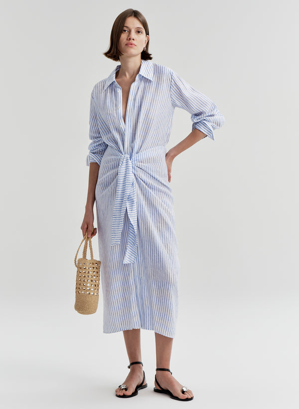 Woman wearing a blue and white striped dress with a knot detail on a plain background