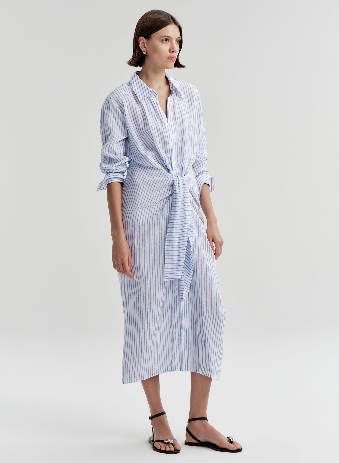 Woman wearing a blue and white striped dress with a knot detail on a plain background