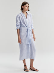 Woman wearing a blue and white striped dress with a knot detail on a plain background