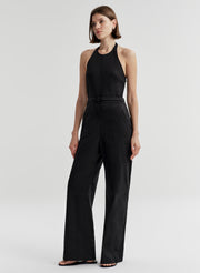 Woman wearing a halter black sleeveless jumpsuit on a light gray background