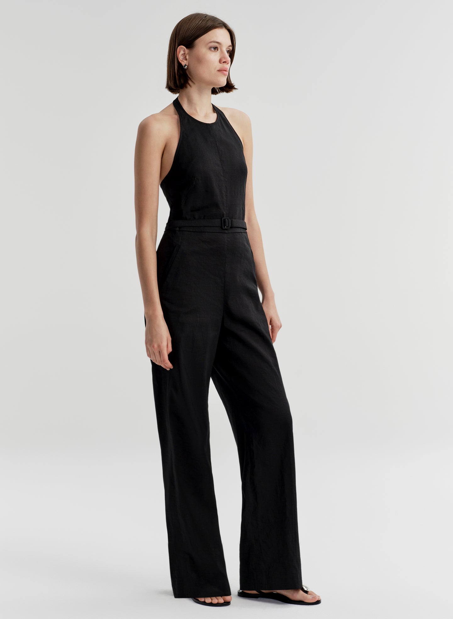 Woman wearing a halter black sleeveless jumpsuit on a light gray background