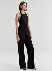 Woman wearing a halter black sleeveless jumpsuit on a light gray background
