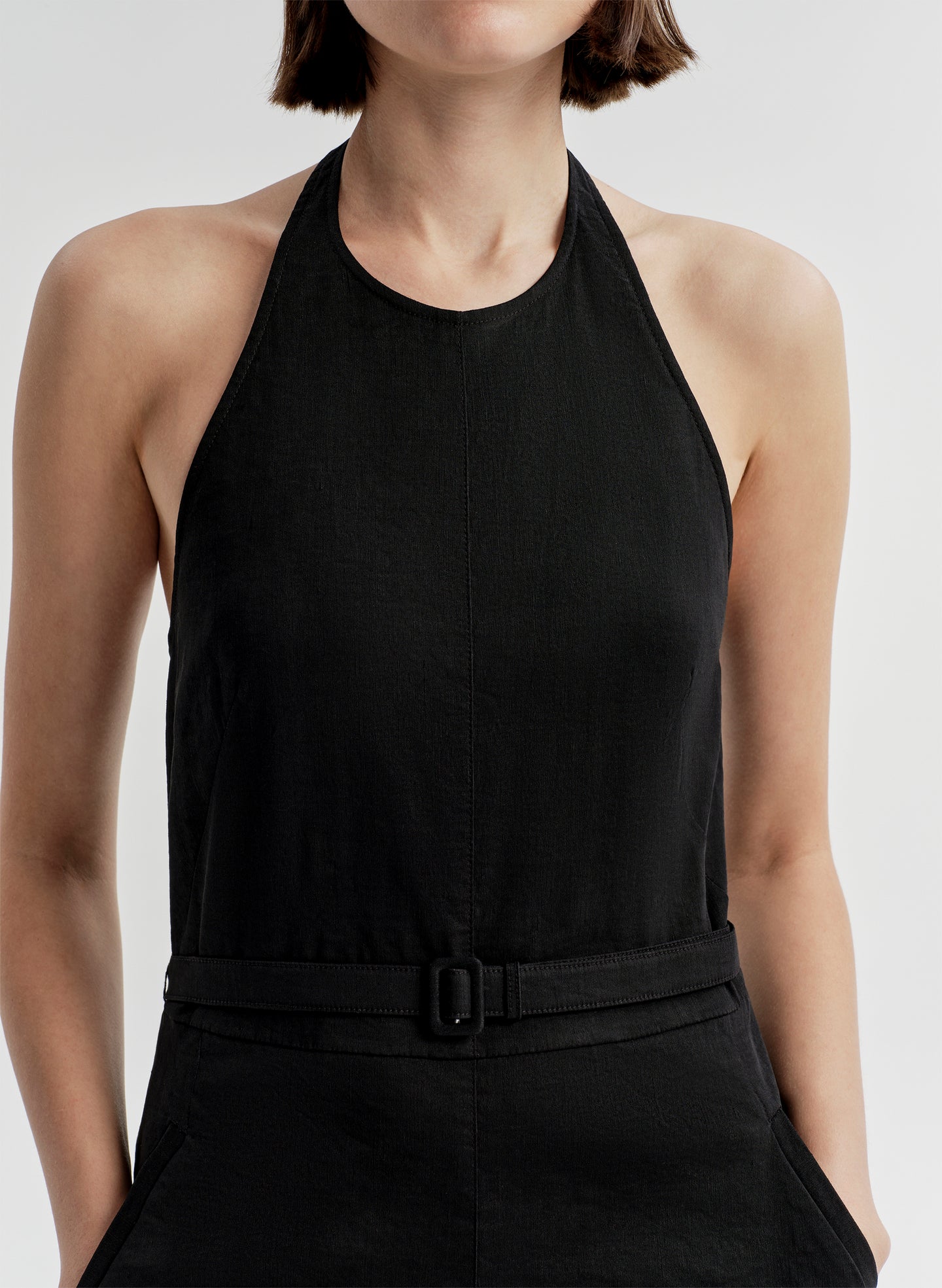 Woman wearing a black halter  jumpsuit on a light gray background