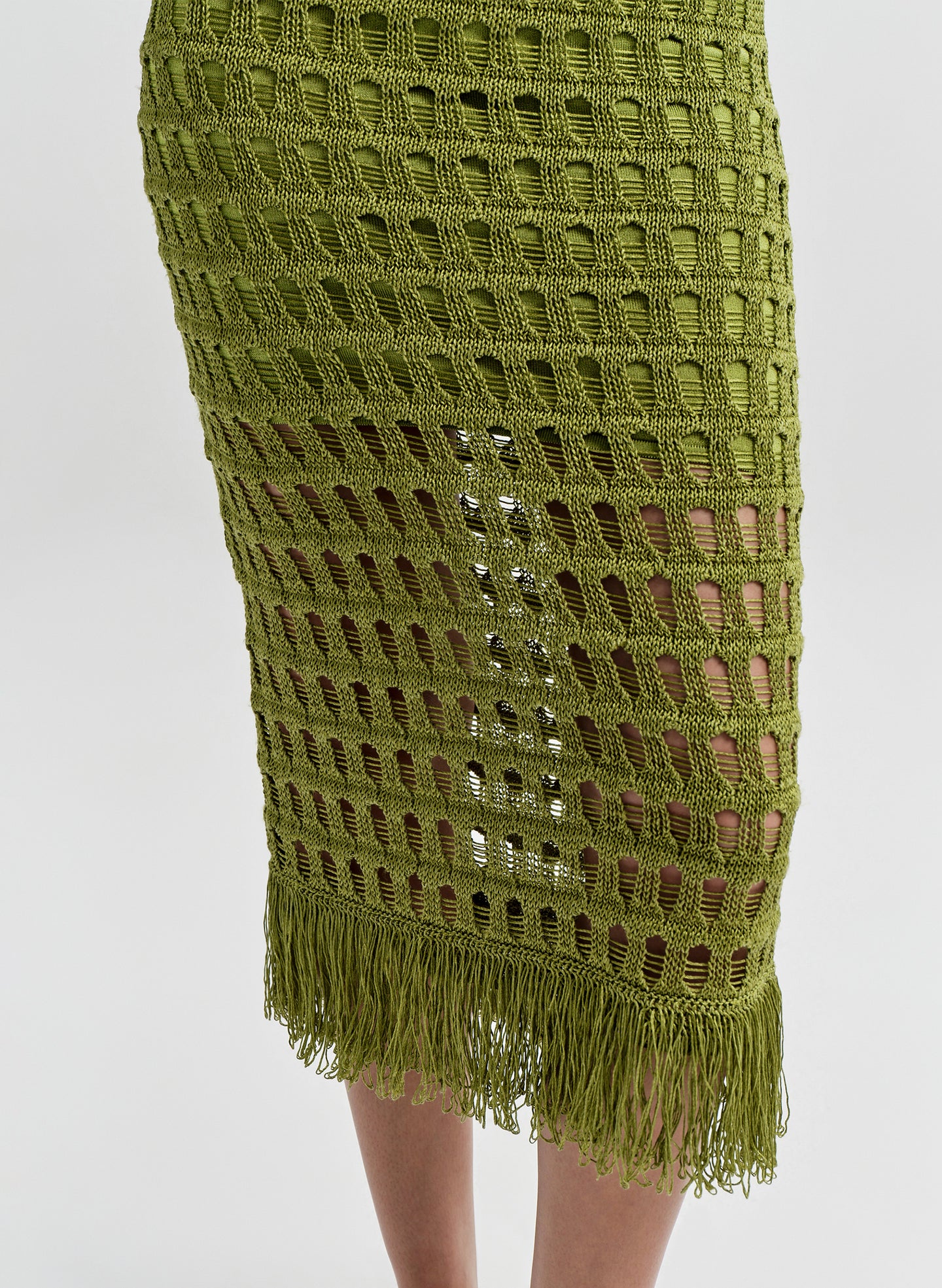 Woman wearing a green crochet dress with fringe detail on a white background