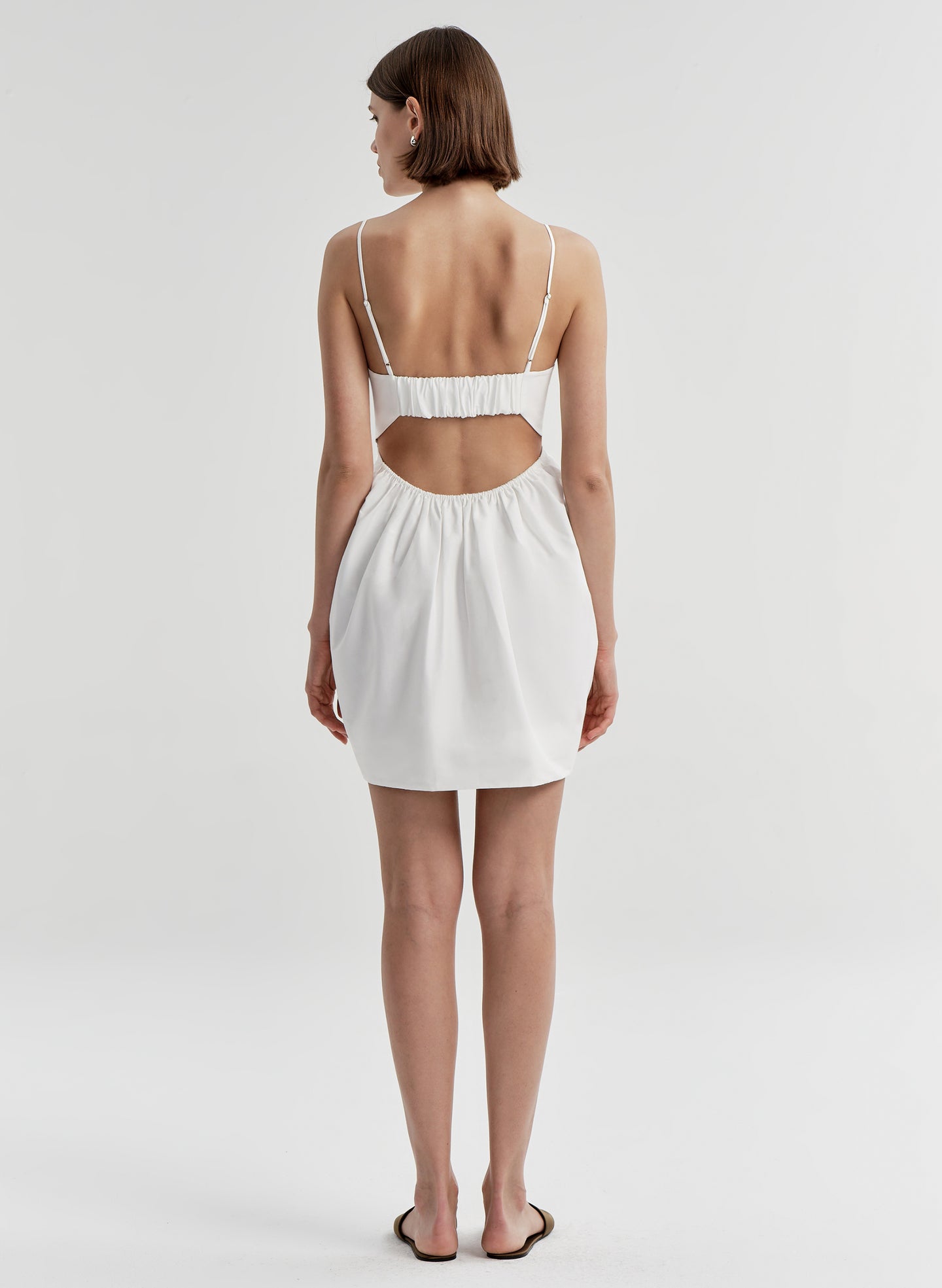 Woman wearing a white dress with cut-out design on a plain background