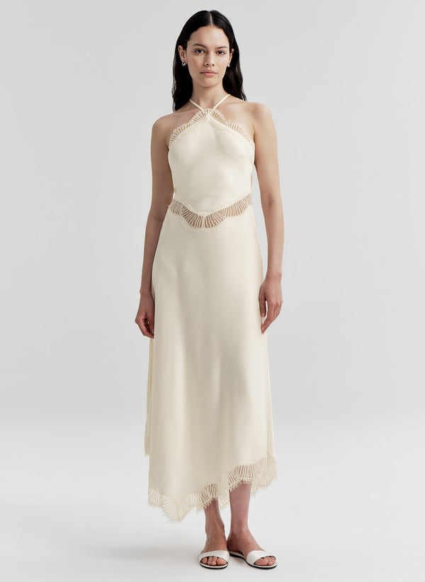 Woman wearing a white halter neck dress with lace waistband on a light gray background