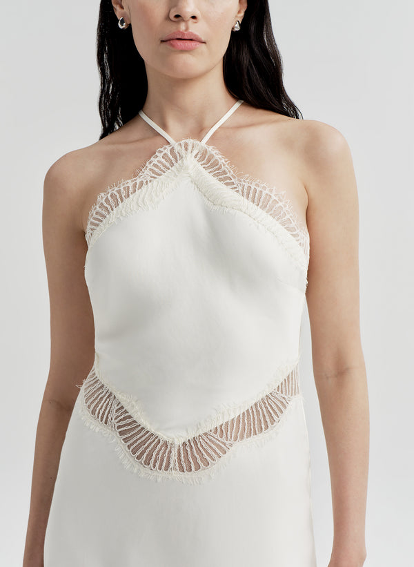Woman wearing a white halter neck dress with lace details on the chest and mid area with a light gray background