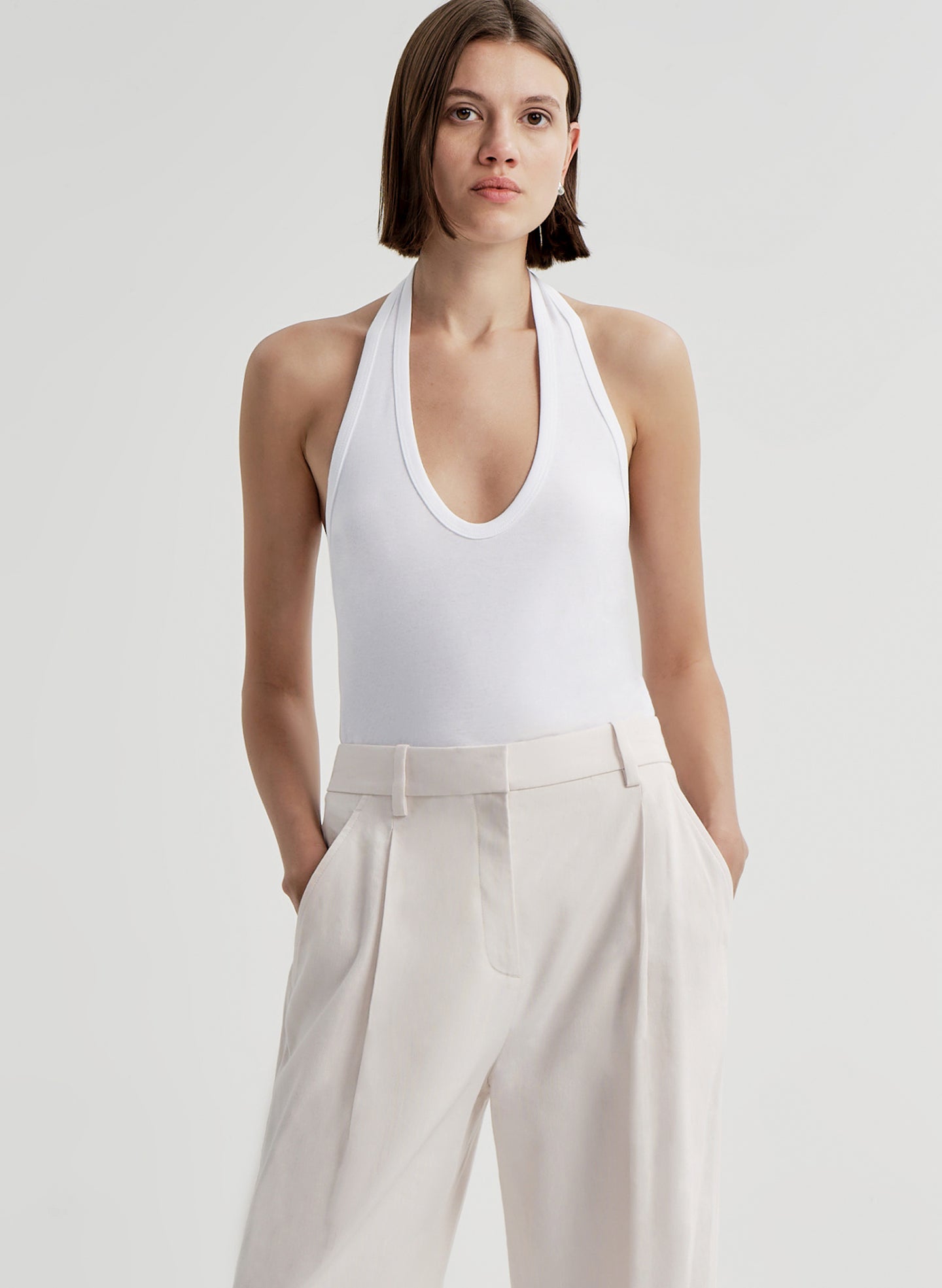 Woman wearing a white halter top and light-colored pants on a plain background